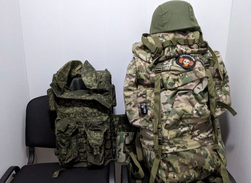 An image depicting military equipment provided to Wagner Group recruits. It includes a military rucksack, a standard issue military helmet, and body armor. The rucksack is designed for carrying essential supplies and equipment during military operations, while the helmet and body armor offer protection to the wearer in combat situations.