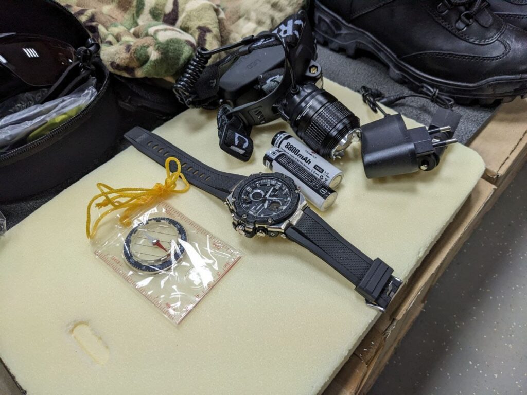 An image showcasing a military watch and compass issued to new Wagner Group recruits. The military watch is rugged and designed for tactical use, featuring multiple functions and a durable wristband.